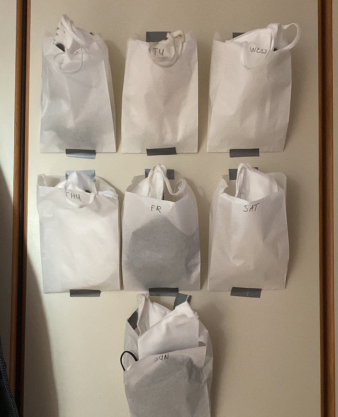 Photo of seven paper bags marked with the days of the week, as an example of how to store and reuse masks.